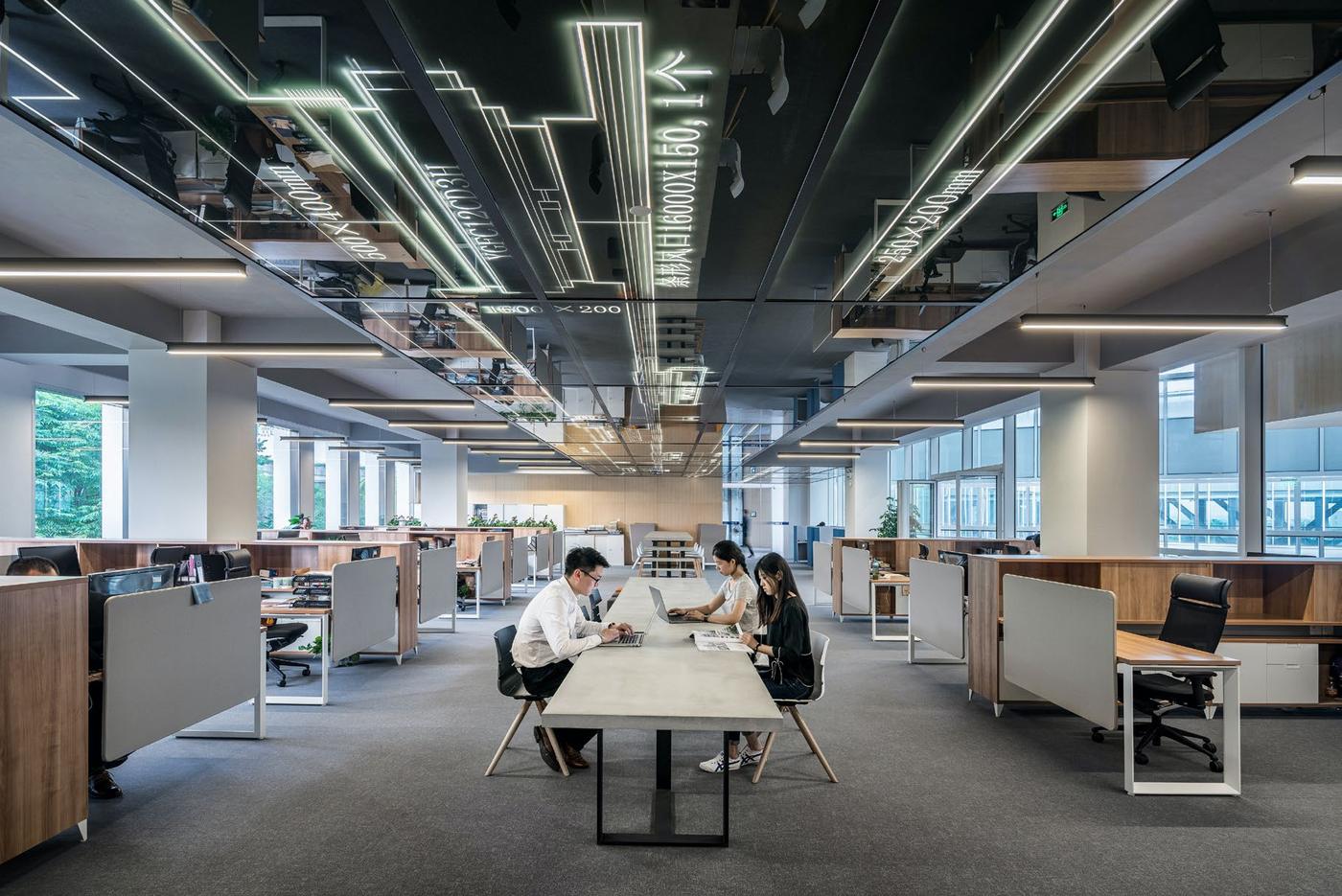 Vista ampla de um escritório corporativo com estações de trabalho e uma equipe reunida ao centro.